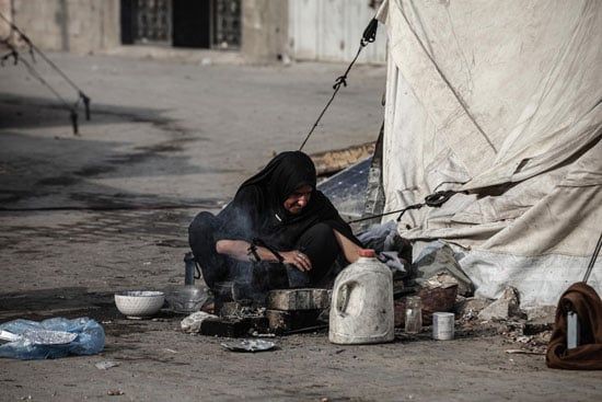 سيدة تحاول أشعال النيران لعمل كوب شاى وسط الخيام فى مخيم البريج