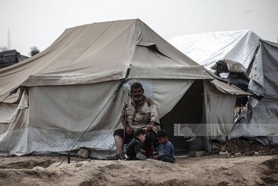 مسن فلسطينى يجلس بجوار الأطفال وسط الخيام