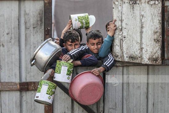 أطفال يحملون الأوانى للحصول على الطعام